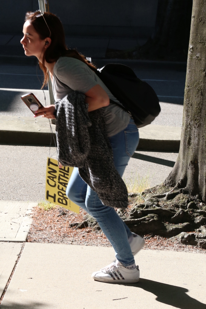 A person in gray grabbing a sign on a sidewalk wrote, "I cant breathe".